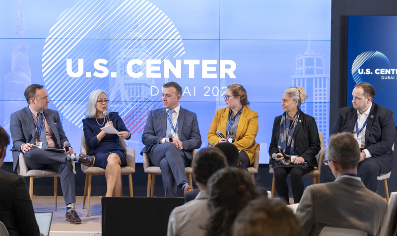  Six women sit in chairs on a stage for a panel discussion.
