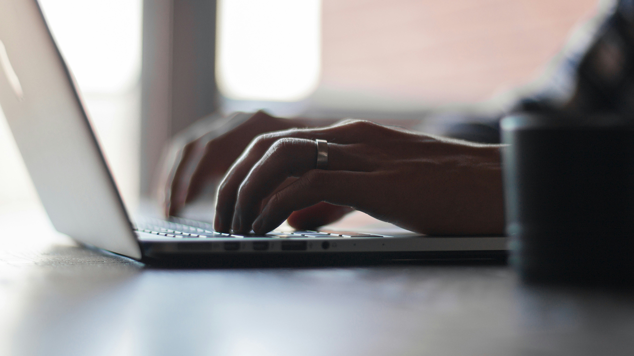 Close-up of hands typing on a laptop at a desk