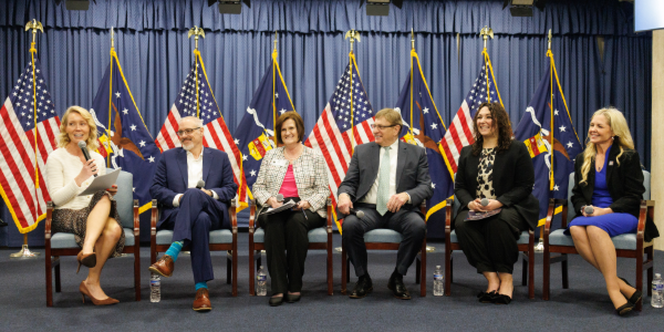 Ten people in professional clothes hold signed documents while posing for a photo. Flags of the United States and the Labor Department are visible behind them. 