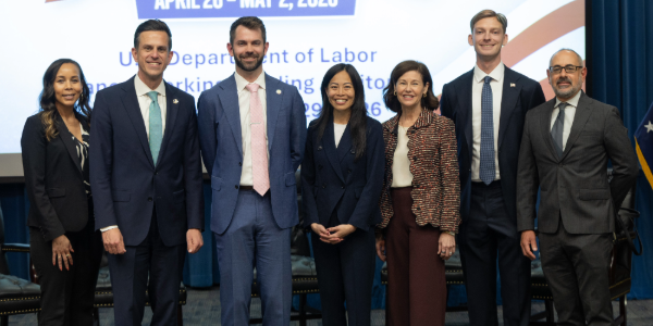 Seven men and women in professional clothing pose for a group photo in front of a screen.