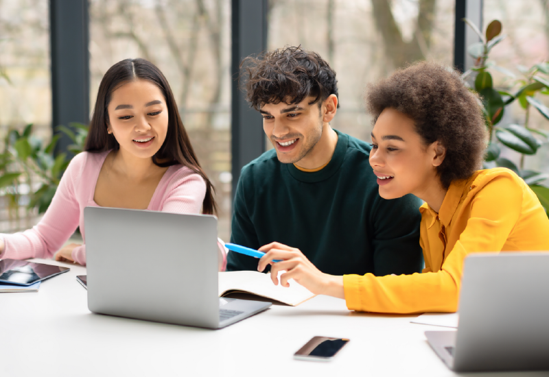 Three students look at a laptop.