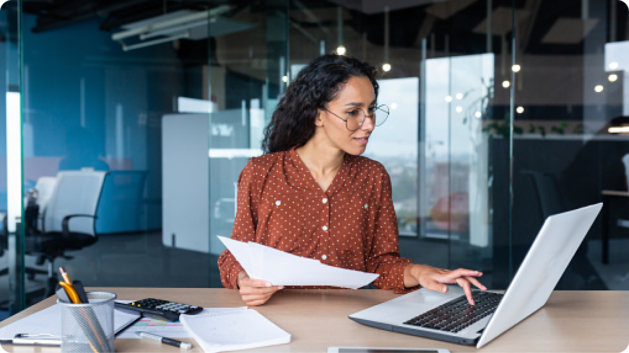 Woman reviewing documents on a laptop in an office setting.