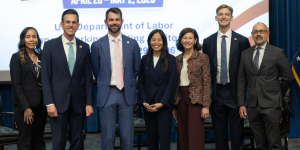 Seven men and women in professional clothing pose for a group photo in front of a screen.