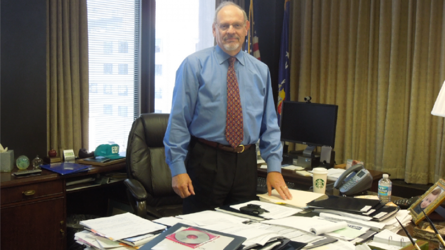 Alan Lebowitz standing behind a desk covered with papers relating to his work at EBSA