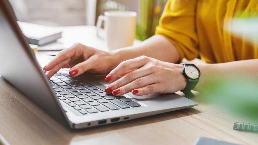 Close-up of a person typing on a laptop at a desk in a home office
