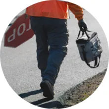 A construction worker carries a stop sign in one hand and a lunch box in the other