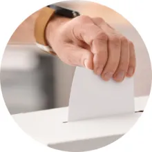 Close-up of a hand inserting a paper ballot into a box