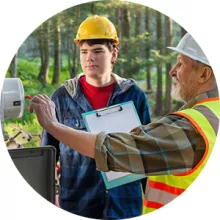 Two workers examine electrical equipment outside