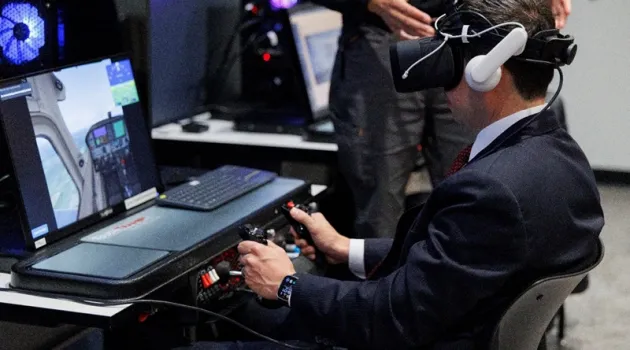 A man in a suit uses a virtual reality headset and aircraft controls as part of a pilot training simulation.