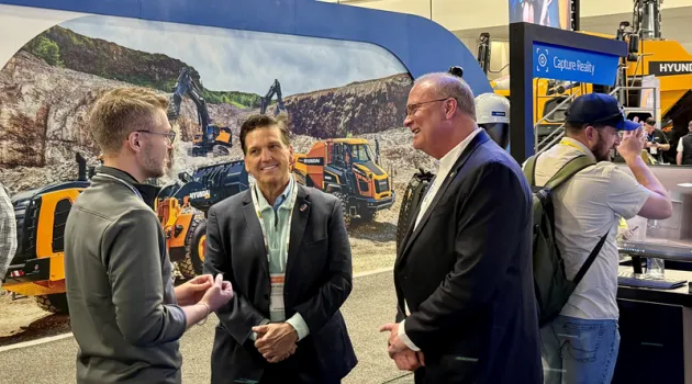 Several men speaking in front of a construction display at an industry expo.