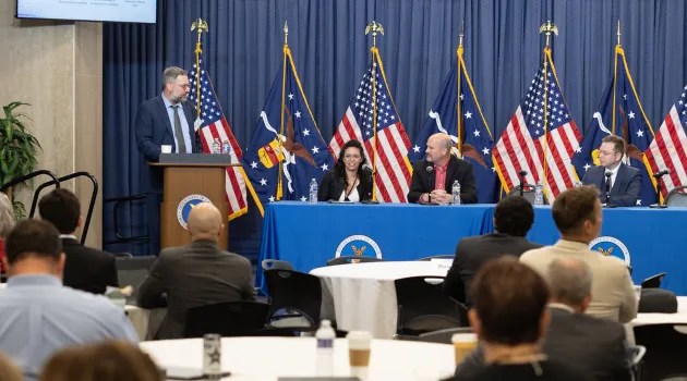 One person stands behind a podium and several sit at a table with microphones during a panel discussion at the U.S. Department of Labor. 