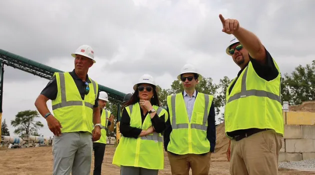 Keith Sonderling and Lori Chavez-DeRemer stand on a construction site with workers, all wearing safety vests and hard hats.