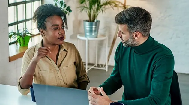 a woman and a man sitting behind a laptop computer and having a discussion