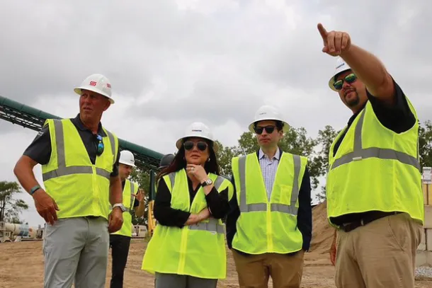 Keith Sonderling and Lori Chavez-DeRemer stand on a construction site with workers, all wearing safety vests and hard hats.
