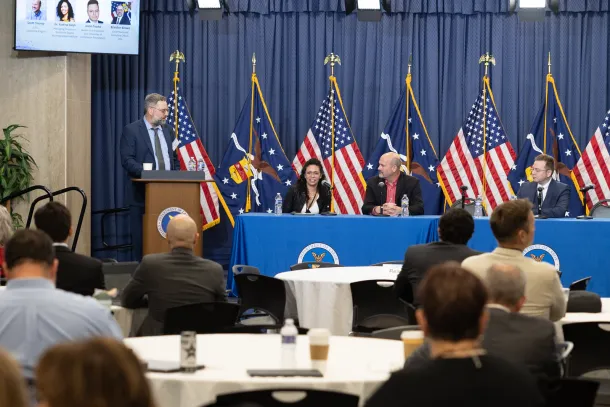 One person stands behind a podium and several sit at a table with microphones during a panel discussion at the U.S. Department of Labor. 
