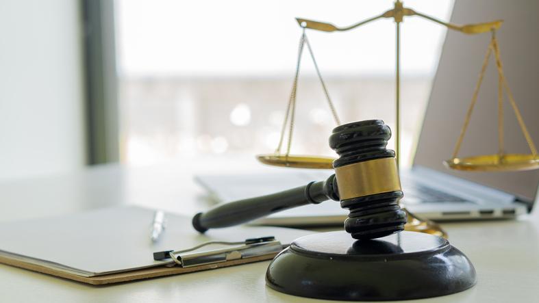 A desk with a laptop, clipboard, a judge's hammer and the scales of justice.