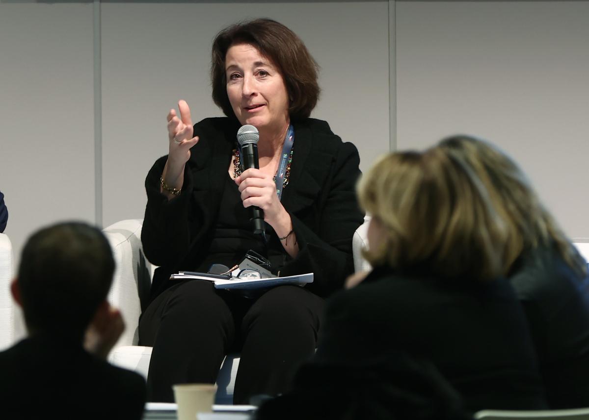 A woman with short brown hair holds a microphone while speaking during a forum.