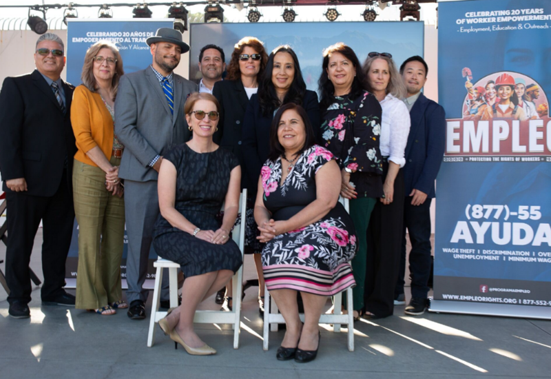 Eleven people in business attire pose in front of an EMPLEO program banner with the hotline.