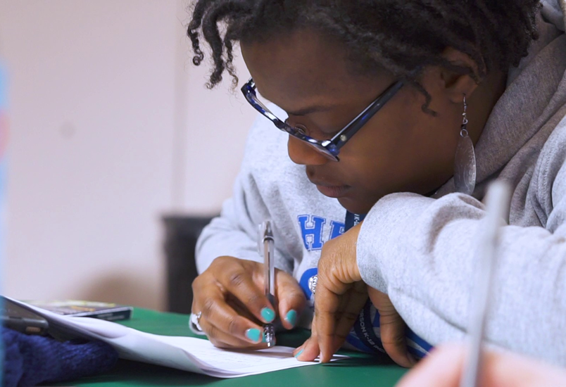 A woman fills out paperwork at a desk.
