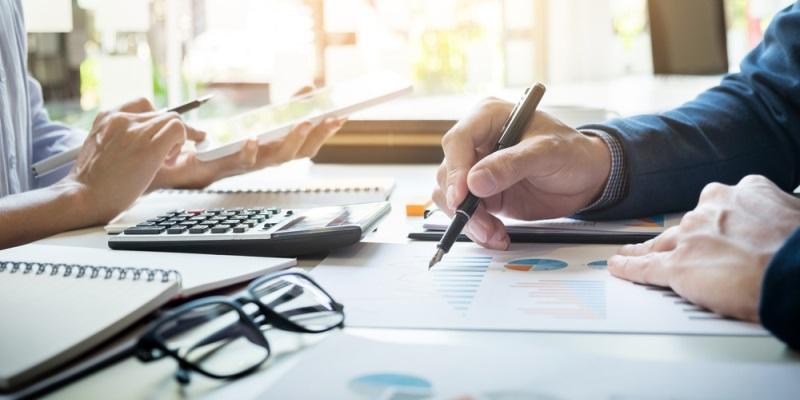 A man and woman sit at an office table, reviewing documents containing data. 