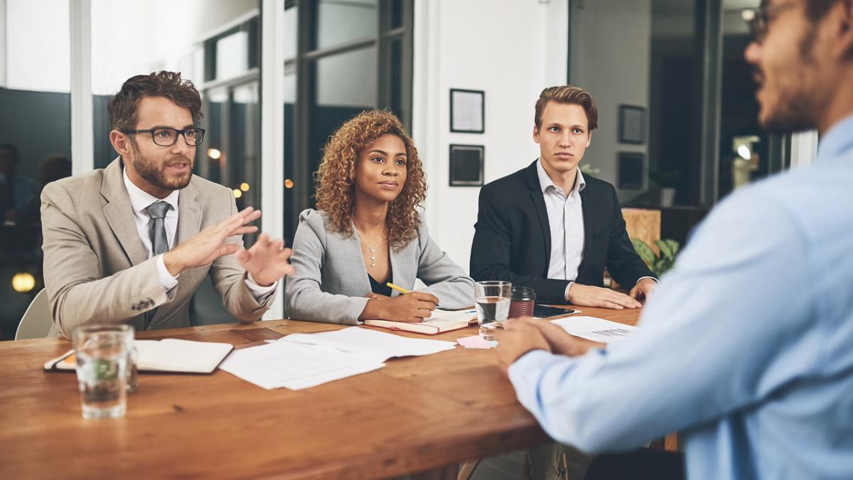 Three businesspeople interview a job candidate across a table in an office