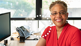 a smiling woman wearing a red shirt sitting at her desk