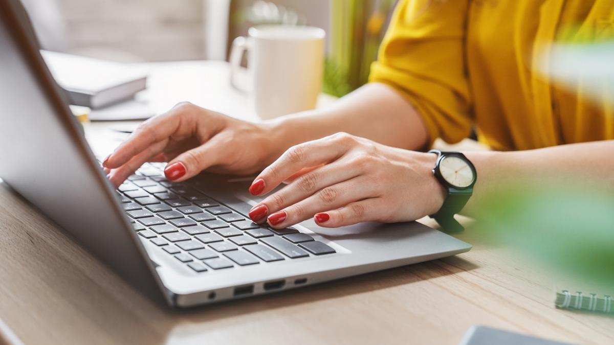 Close-up of a person typing on a laptop at a desk in a home office