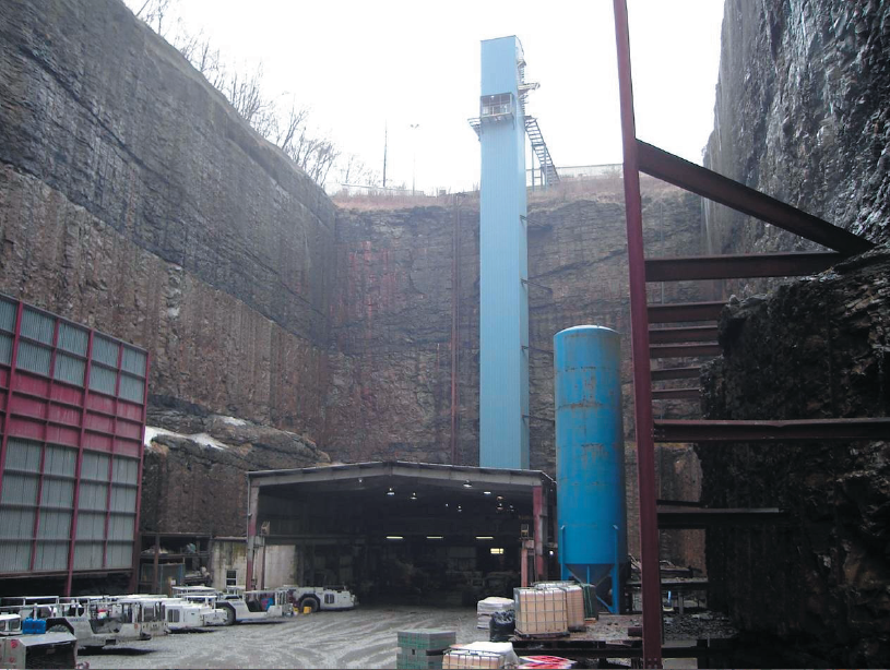 Within a small canyon there is a large covered entrance to the Aracoma mine. Vehicles of different types and sizes are parked outside.
