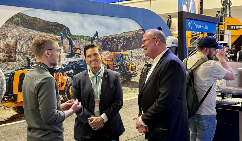 Several men speaking in front of a construction display at an industry expo.