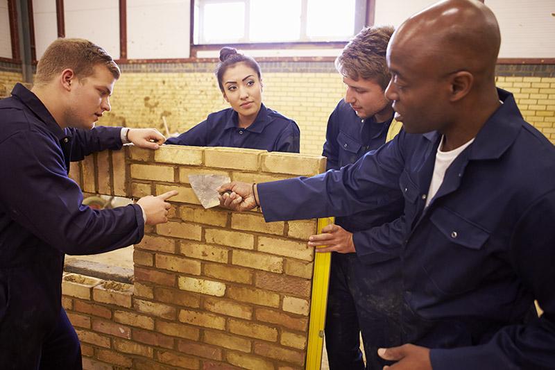 Four apprentices building a brick wall