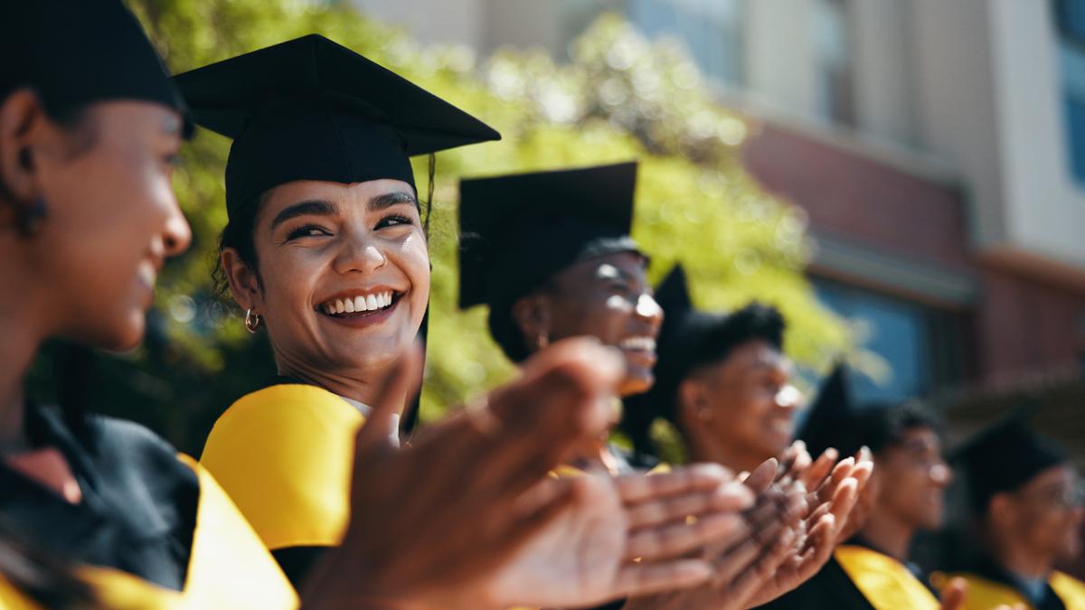 Students in graduation caps and gowns applaud during an outdoor university graduation ceremony